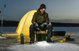 beste-ledbar.no - Kraftig hodelykt best i test og faktasjekk: Mann isfisker i mørket foran teltet sitt på vinteren, og har en kraftig hodelykt på hodet som lyser opp arbeidsområdet.